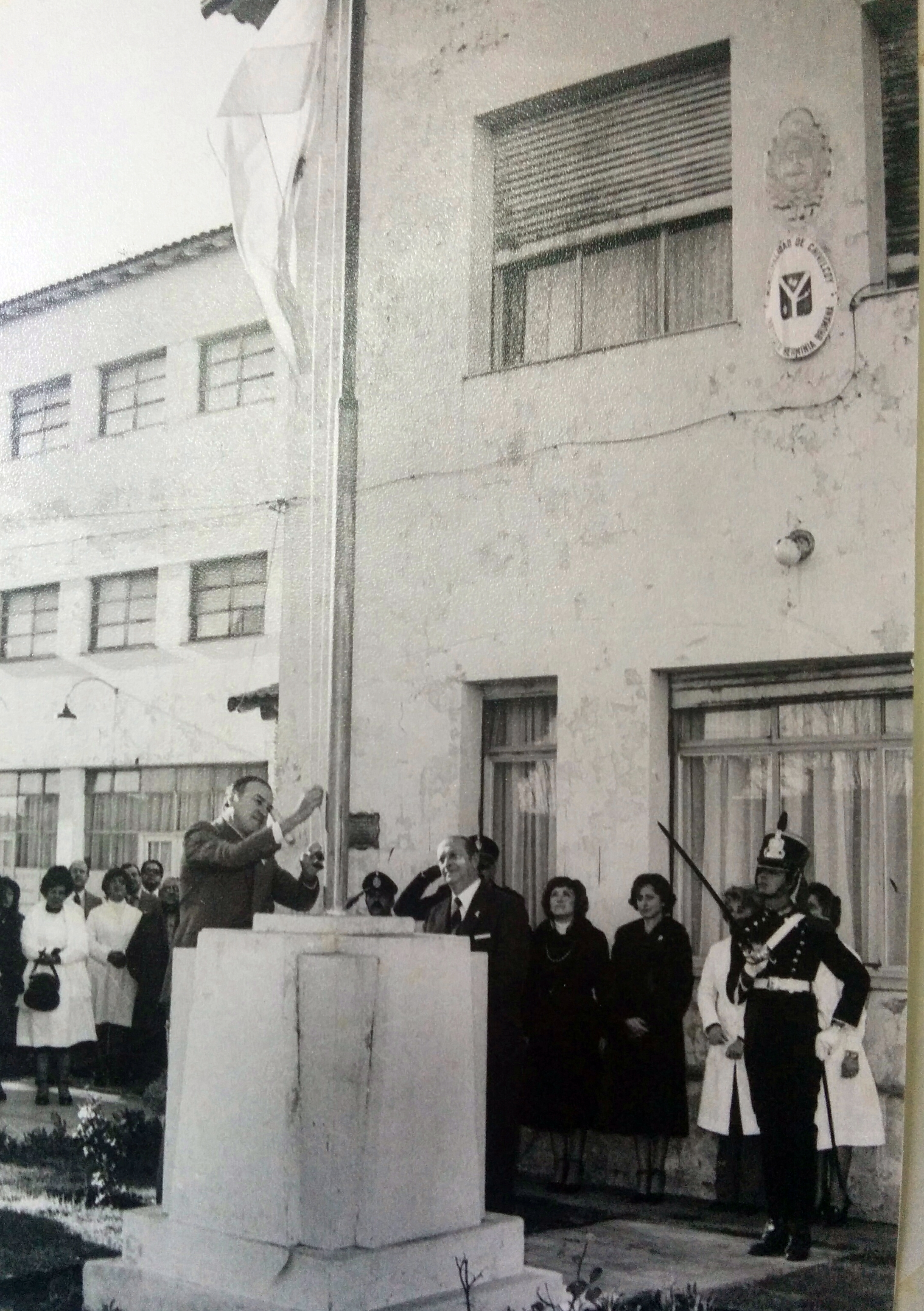 El secretario de Gobierno de la comuna, e intendente municipal interino, agrimensor Héctor Miguel Massino, al izar la bandera, en el mástil del Instituto Brumana, antes del comienzo de una ceremonia oficial. Año 1980.